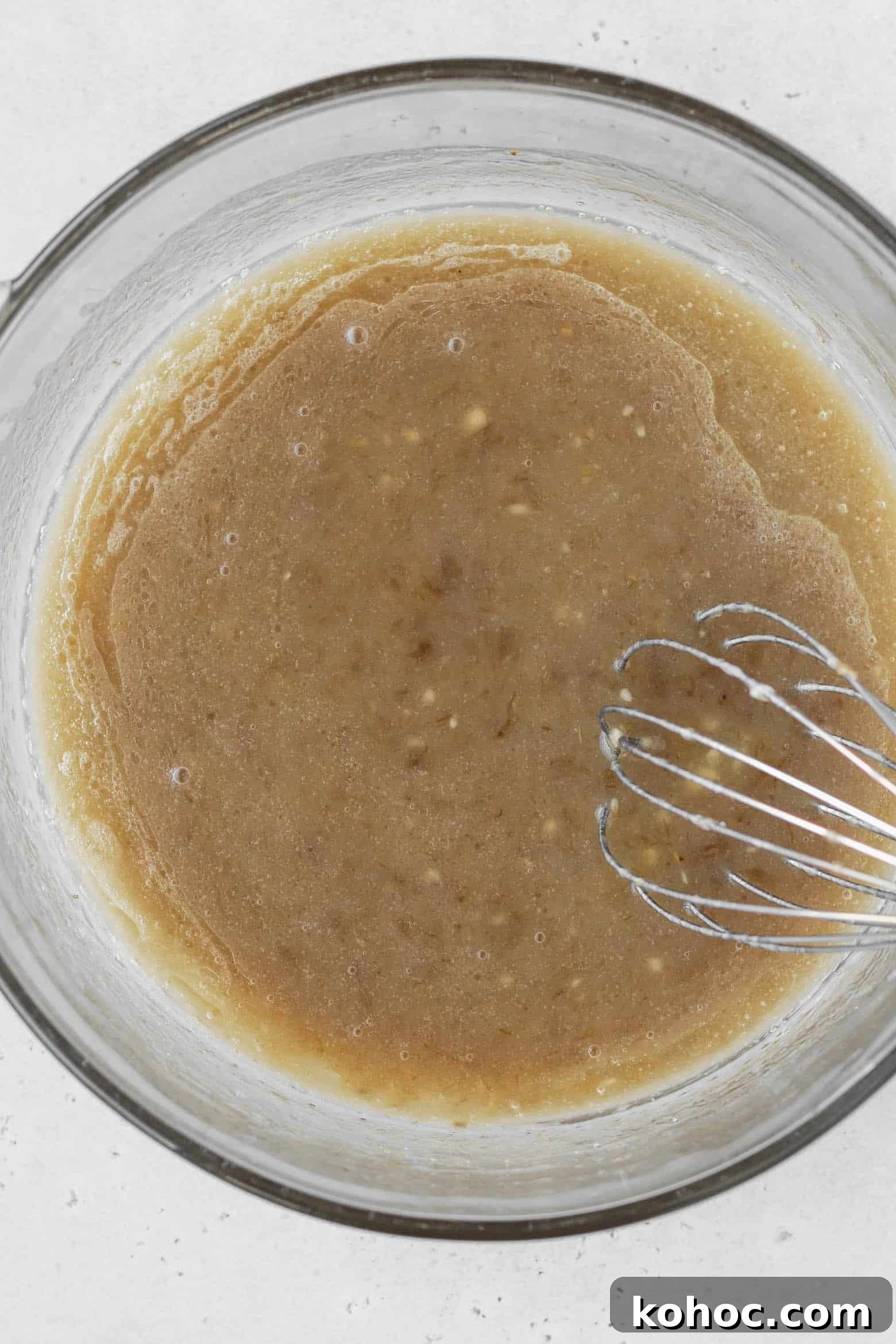 A bowl of oil, mashed banana, sugar, and vanilla extract mixed together.