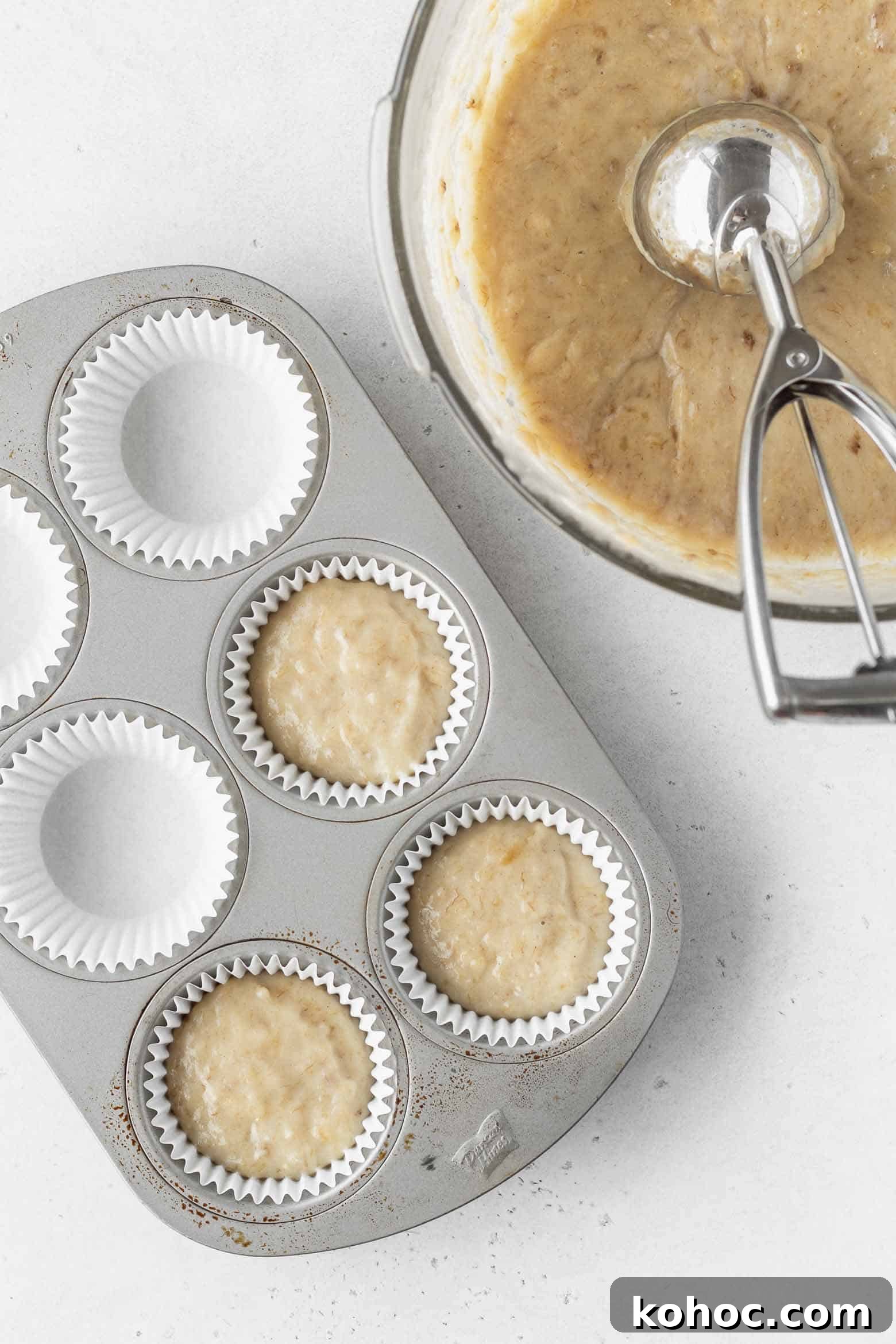 Vegan banana cupcake batter scooped into a cupcake pan using an ice cream scoop.