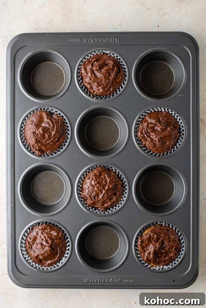 chocolate muffin batter in muffin liners in every other whole of a muffin pan
