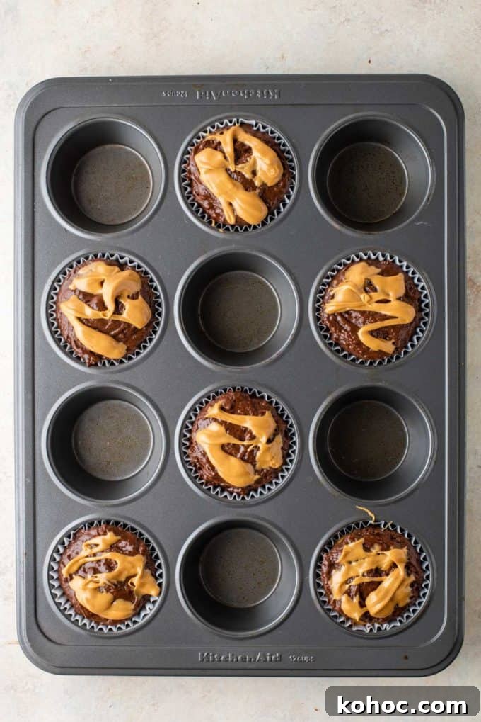 chocolate muffin batter with peanut butter on top in muffin liners in every other whole of a muffin pan