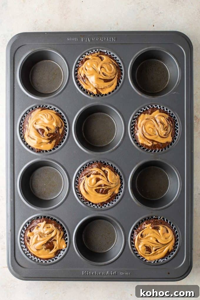 chocolate muffin batter with peanut butter on top in muffin liners in every other whole of a muffin pan