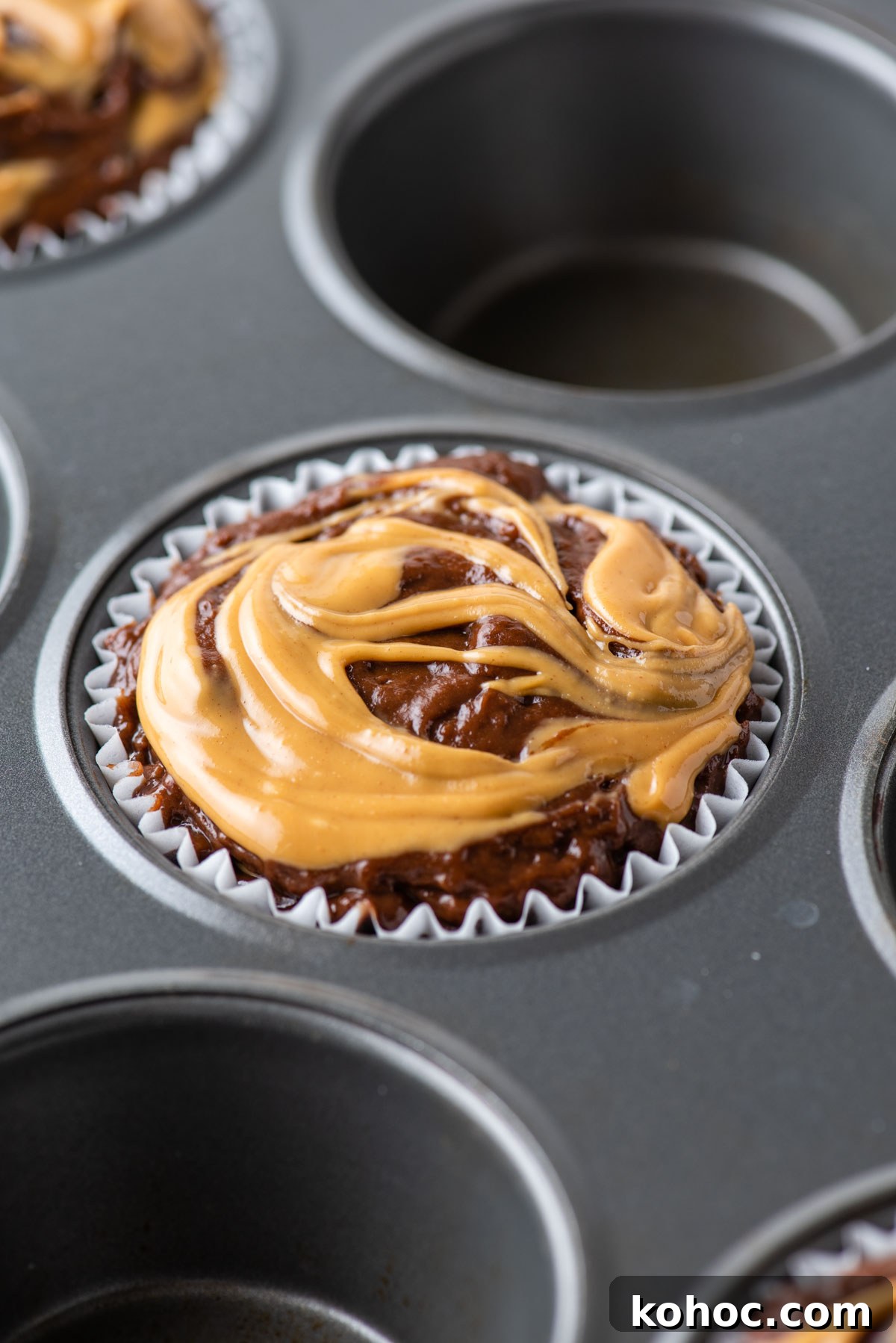 chocolate peanut butter muffin batter with peanut butter on top in a muffin tin