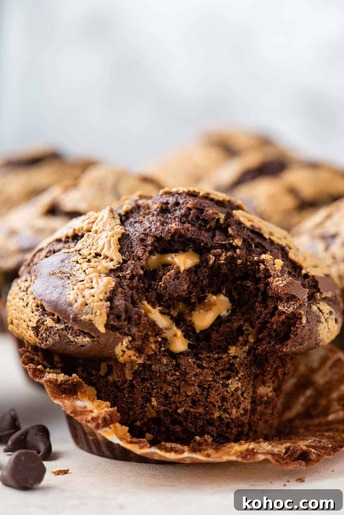 chocolate peanut butter muffins with the one closest having its muffin liner pulled partially off and a bite taken out