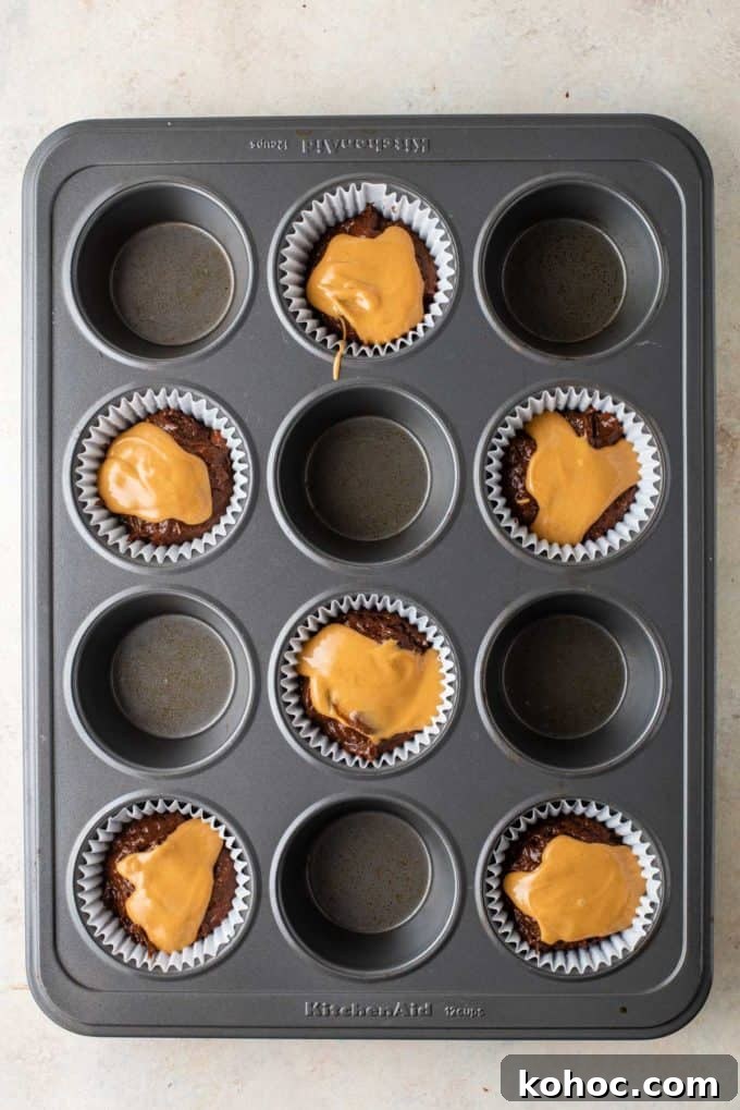 chocolate muffin batter with melted peanut butter on top of it in muffin liners in every other whole of a muffin pan