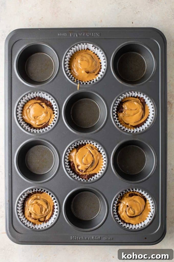 chocolate muffin batter with melted peanut butter on top of it in muffin liners in every other whole of a muffin pan