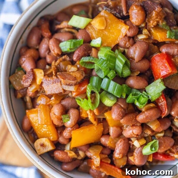 A bowl of delicious Mexican beans mixed with diced bell peppers, onions, and topped with chopped green onions.