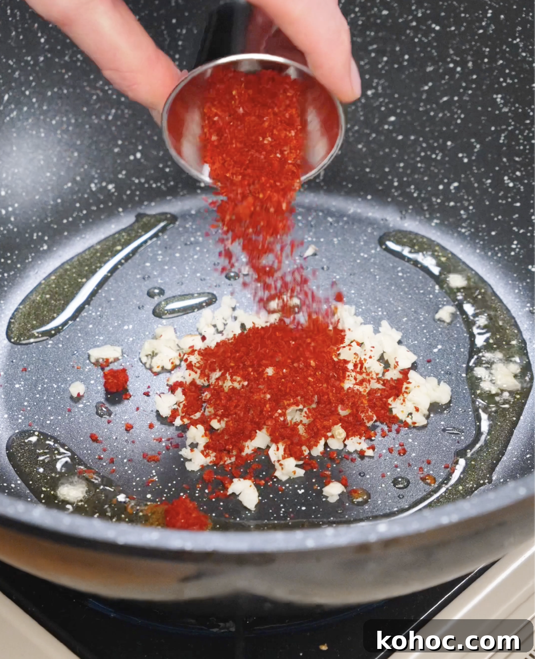 Chili flakes being poured into a pan with minced garlic and oil to begin making garlic chili noodle sauce.