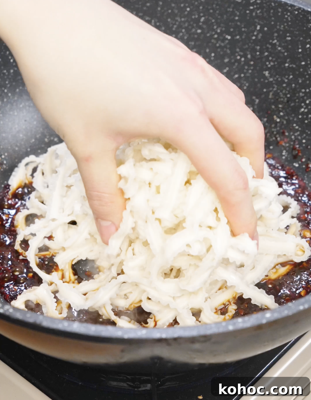 Cooked noodles being added into a pan of spicy chili garlic sauce.