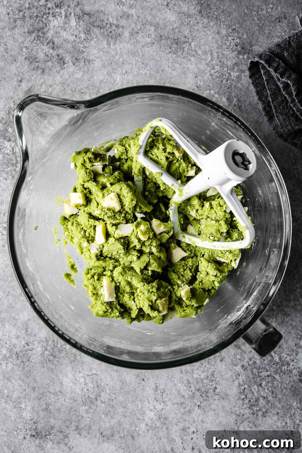 Matcha White Chocolate Cookies Recipe for Soft, Chewy Treats 8 Green cookie dough in a glass mixer with white chocolate chunks added in.