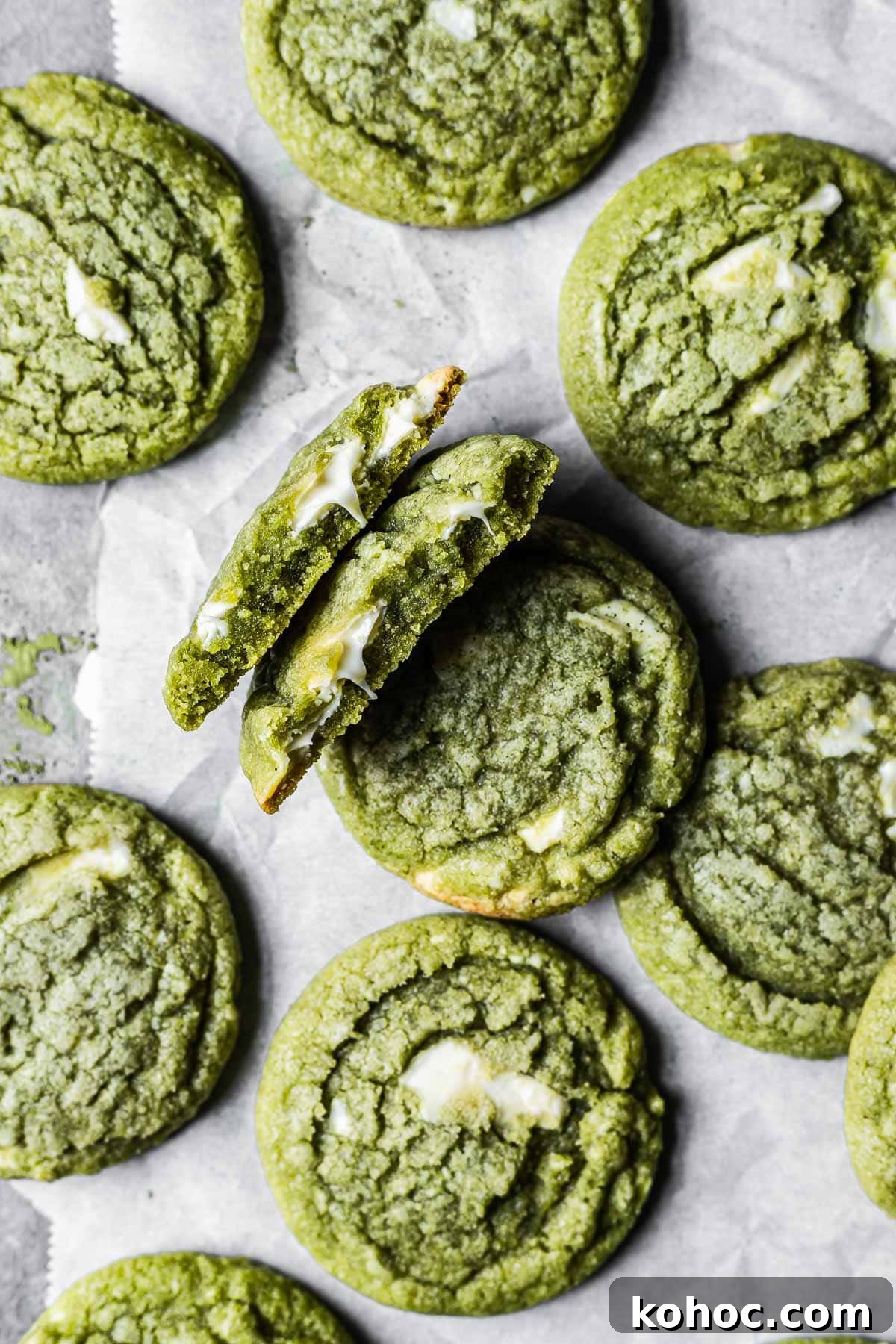 Matcha White Chocolate Cookies Recipe for Soft, Chewy Treats 10 A matcha white chocolate cookie is broken in half, revealing the gooey melted chocolate inside. There are many other matcha cookies surrounding it.
