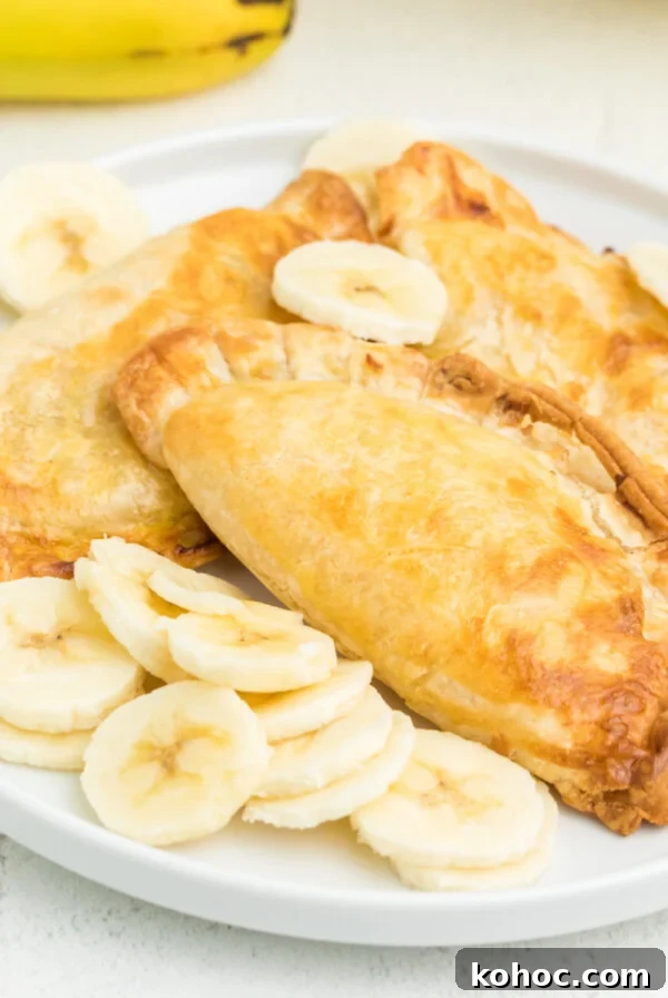 Air fried banana pudding pies on a white plate with sliced bananas.