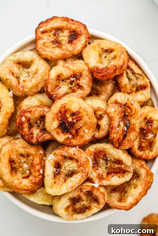 Banana chips made in the air fryer, served in a white bowl with a sprinkling of kosher salt on top.