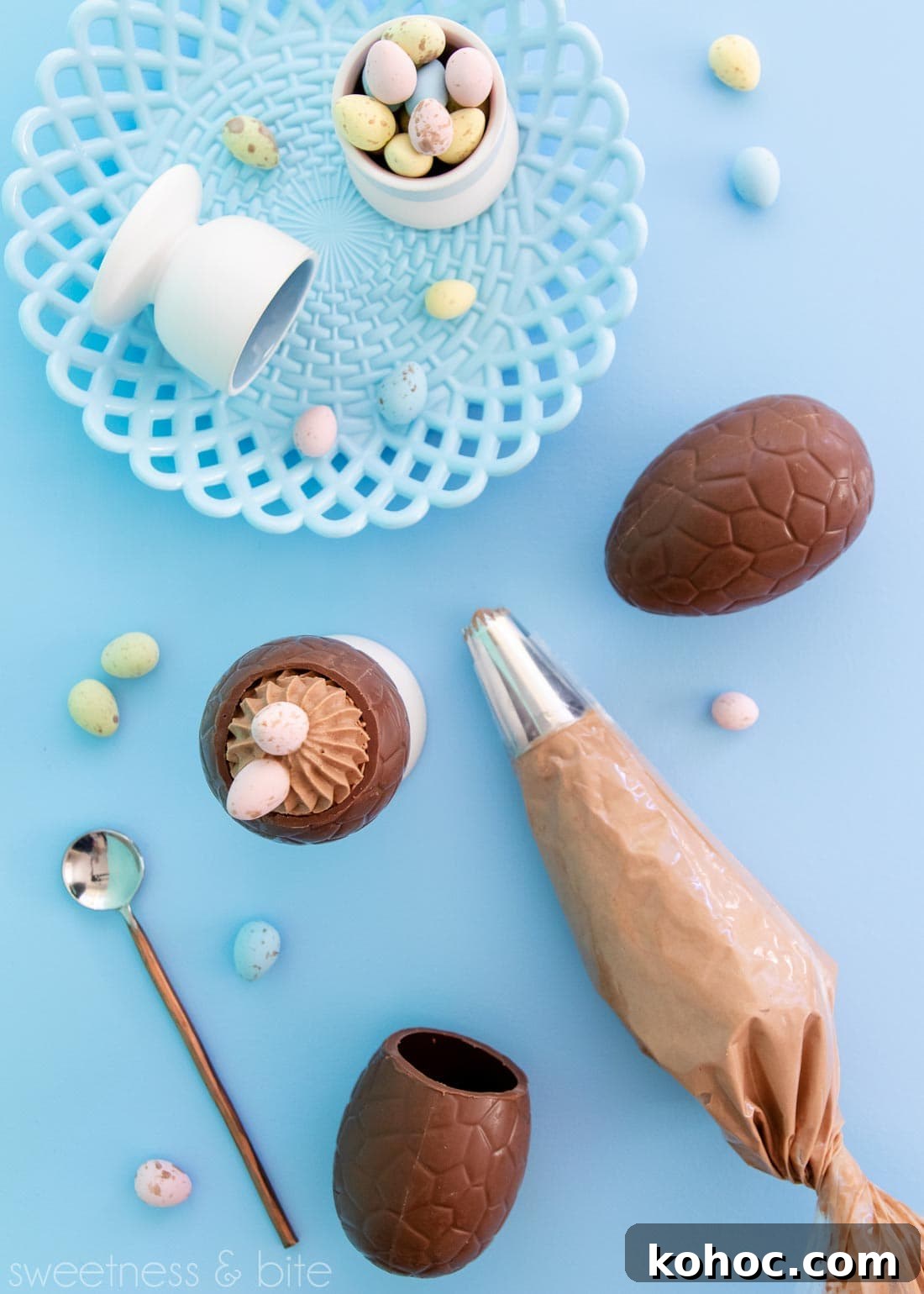 Milk Chocolate Mousse Easter Eggs Recipe for Spring Celebrations 4 Flat lay including a mousse filled egg, piping bag full of mousse, a blue plate and pastel mini eggs, on a blue background.