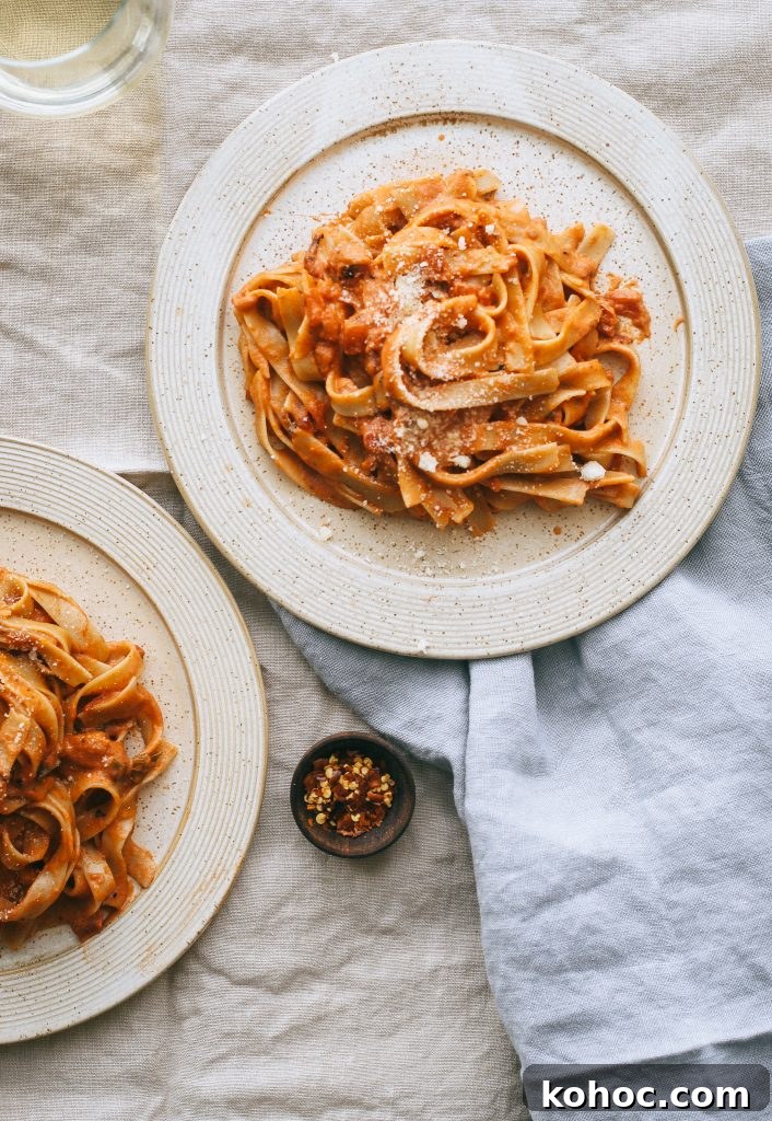 Grandma’s Classic Vodka Sauce Recipe برای Family Gatherings 4 vodka sauce pasta on pale yellow plates with small dish of red pepper flakes and glass of white wine