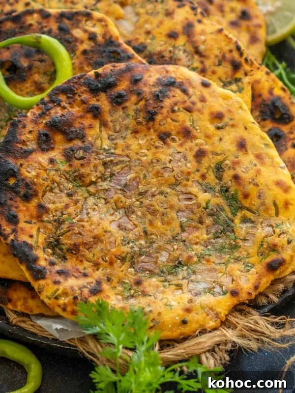 Authentic Bakarkhani Recipe: Flaky Bengali Bread Step-by-Step 20 Three pieces of golden-brown, slightly charred Missi Roti garnished with herbs and onions, served on a rustic plate with green chili, cilantro, and lime slices on the side.