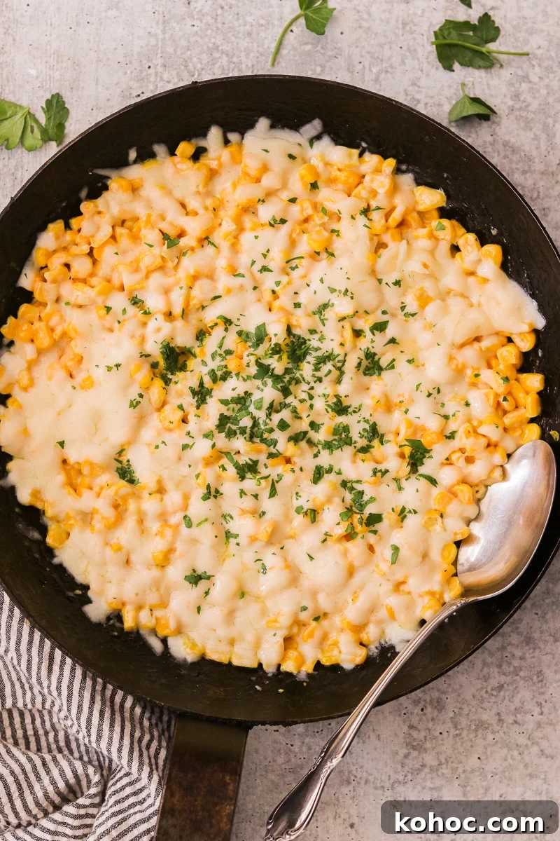 Korean Corn Cheese Recipe: Creamy Baked Koncheese for Sharing 2 Korean corn cheese in a large skillet with a spoon resting inside, topped with melted mozzarella and chopped parsley.