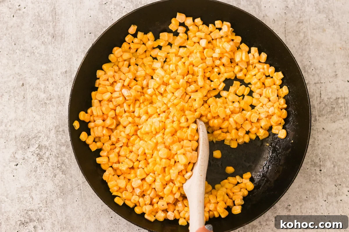 Korean Corn Cheese Recipe: Creamy Baked Koncheese for Sharing 4 Corn kernels cooking in a skillet being stirred with a wooden spoon.