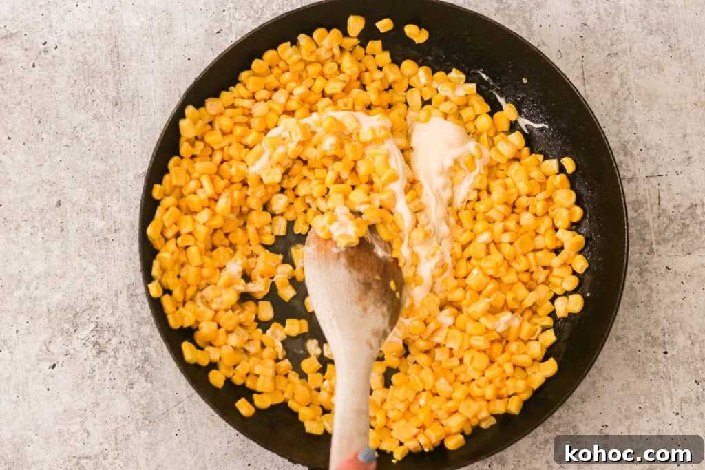 Korean Corn Cheese Recipe: Creamy Baked Koncheese for Sharing 5 Corn mixture in a skillet as sugar and mayonnaise are stirred in with a wooden spoon.
