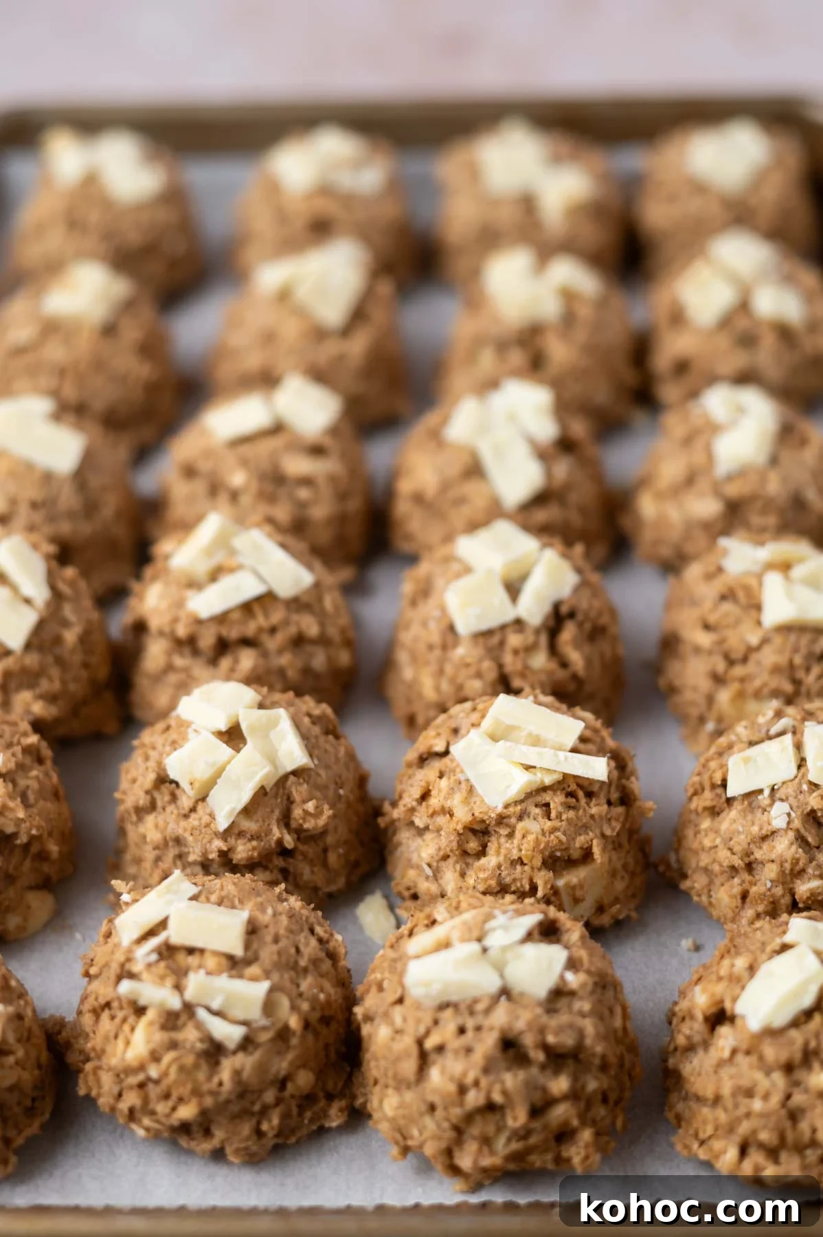 Chewy Brown-Butter Oatmeal Cookies with Sea Salt 7 cookie dough balls with white chocolate on top on a parchment lined baking sheet