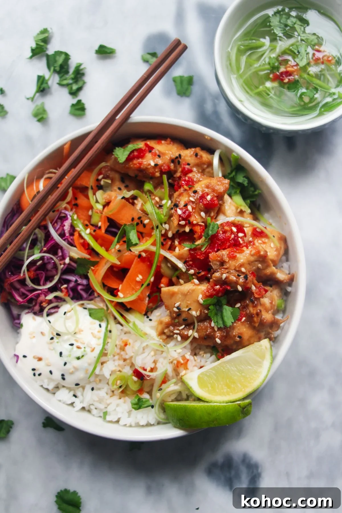 Juicy Chicken Poke Bowl Recipe for Fresh, Flavor-Packed Meals 2 Chicken poke bowl on a grey marble background, with chopsticks on the side and a bowl of curly spring onions behind.