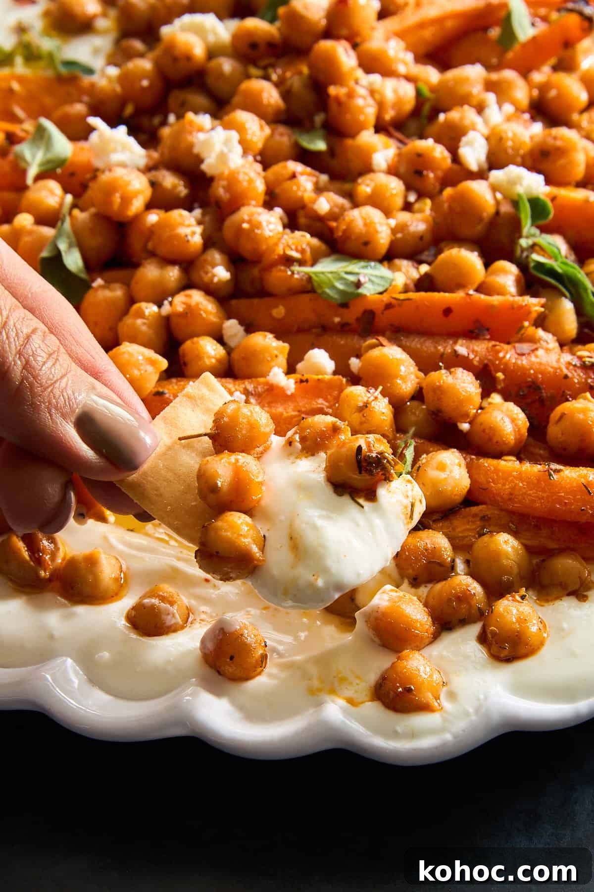 Roasted Carrots & Chickpeas with Creamy Whipped Feta 8 A hand dipping a pita chip into chickpeas and roasted carrot whipped feta.