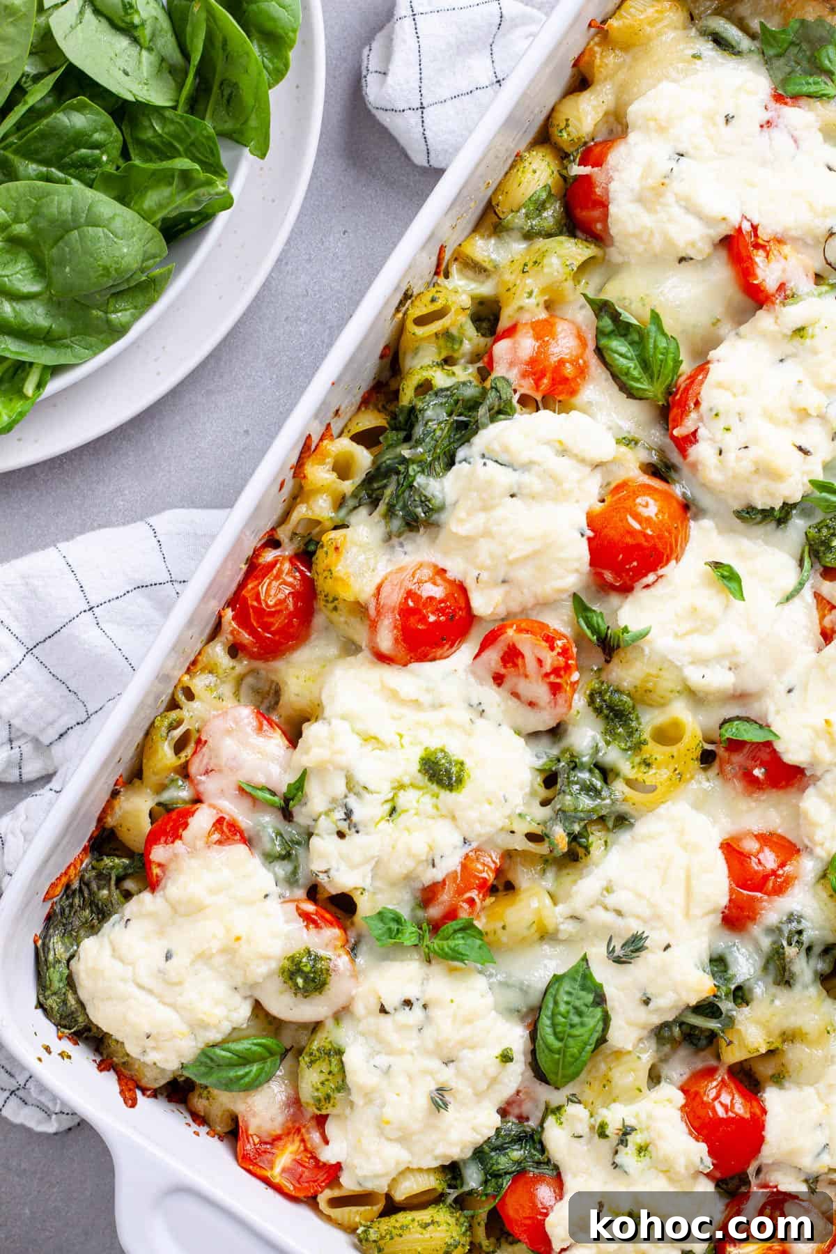 Creamy Baked Ricotta Pesto Pasta with Golden Parmesan Crust 12 A white casserole dish with ricotta pesto pasta topped with mozzarella, tomatoes and spinach.