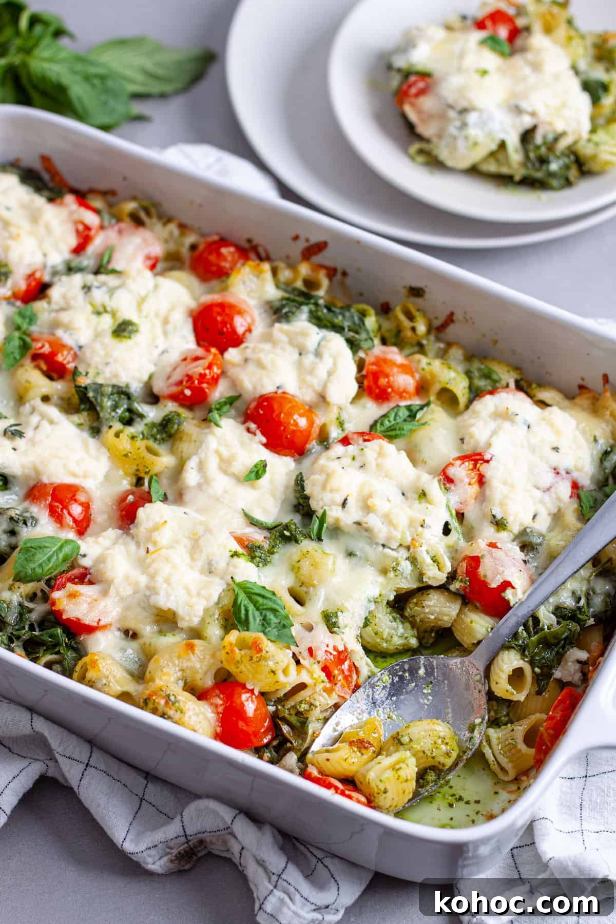 Creamy Baked Ricotta Pesto Pasta with Golden Parmesan Crust 13 A spoon taking a serving of ricotta pesto pasta out of a white casserole dish.