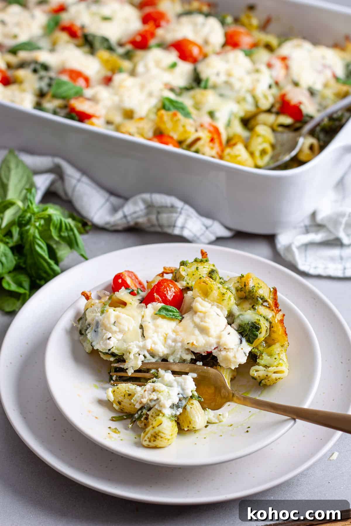 Creamy Baked Ricotta Pesto Pasta with Golden Parmesan Crust 14 A serving of ricotta pesto pasta on a plate with a casserole dish of the baked pasta in the background.