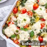 A close up of a baked ricotta pesto pasta topped with tomatoes, spinach and melty cheese.