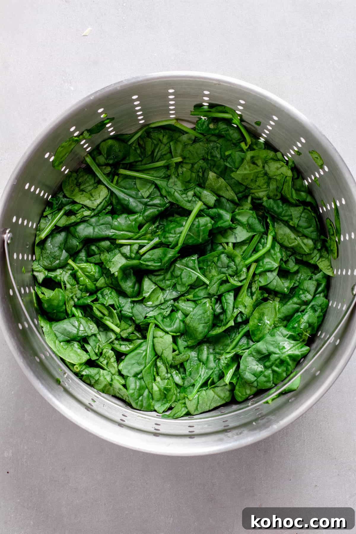 Creamy Baked Ricotta Pesto Pasta with Golden Parmesan Crust 6 Wilted spinach in a strainer on a gray table.