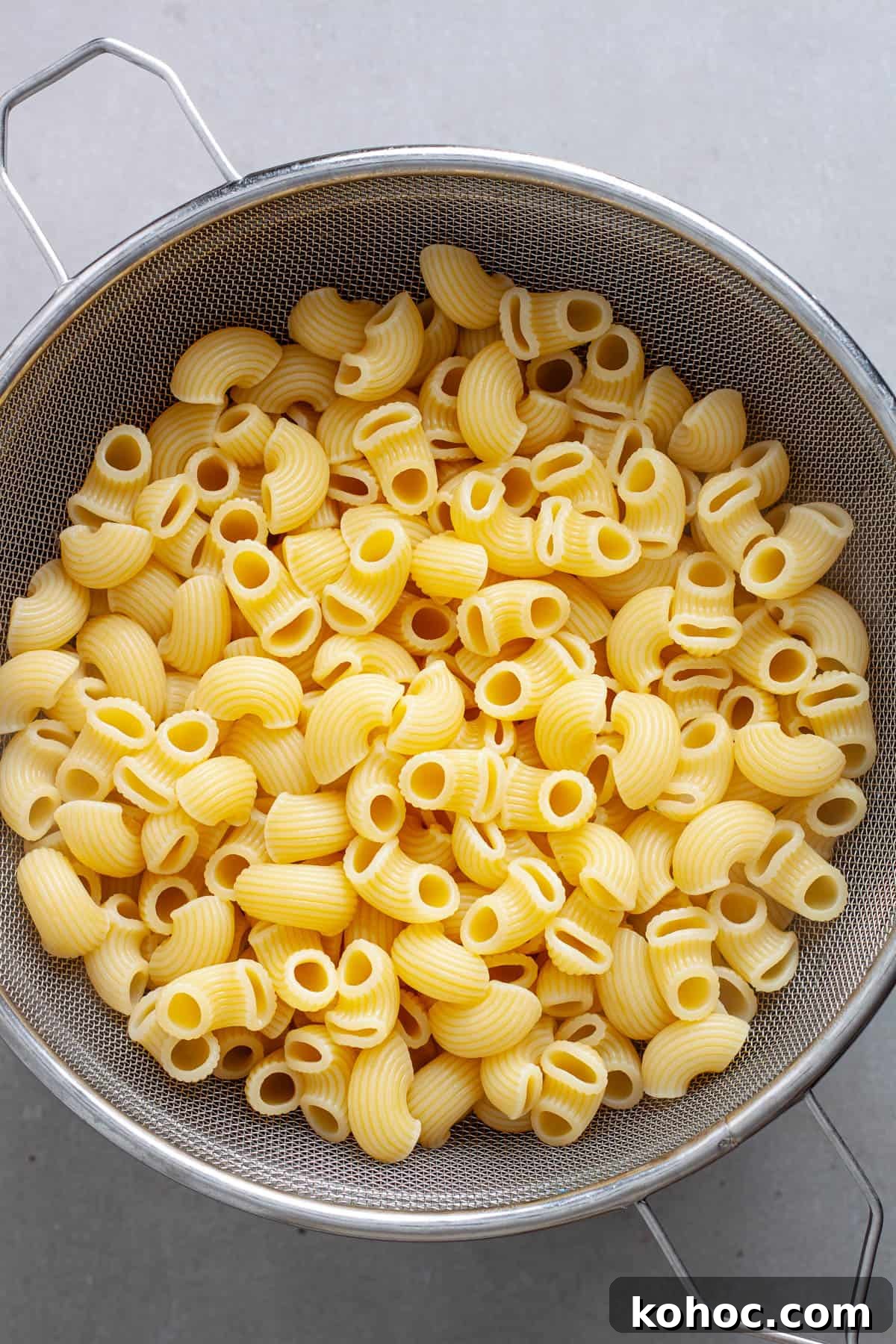 Creamy Baked Ricotta Pesto Pasta with Golden Parmesan Crust 7 Cooked pasta cooling in a strainer on a gray table.