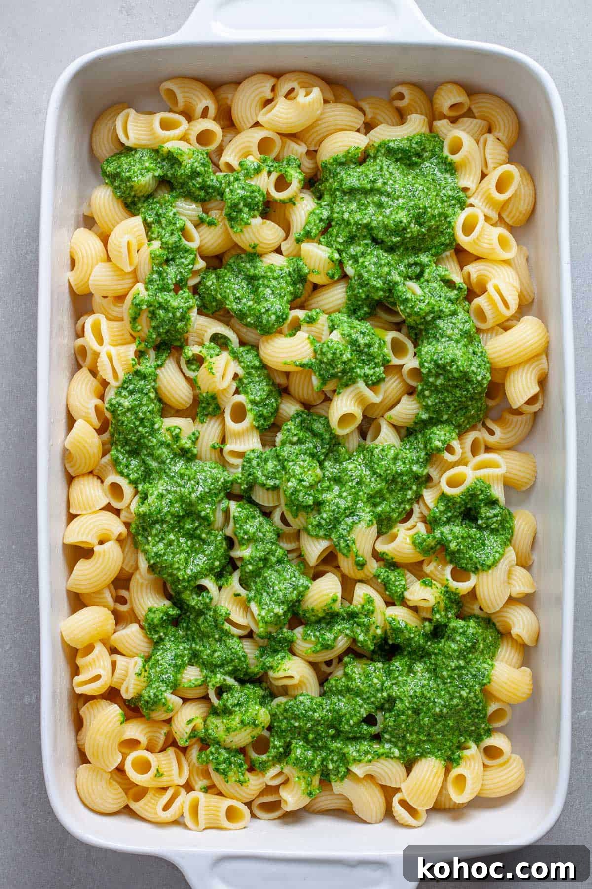 Creamy Baked Ricotta Pesto Pasta with Golden Parmesan Crust 8 A casserole dish of cooked pasta with pesto spooned on top.