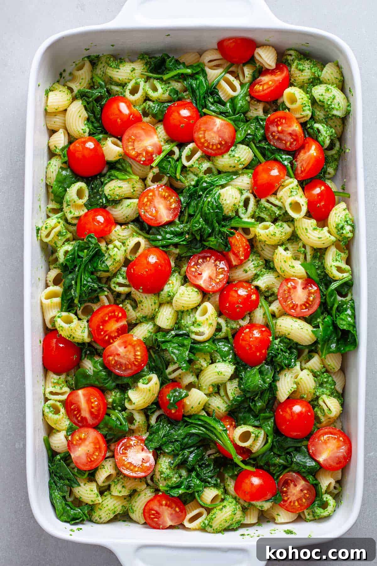 Creamy Baked Ricotta Pesto Pasta with Golden Parmesan Crust 9 Cherry tomatoes and wilted spinach on top of a casserole dish of pasta and pesto.