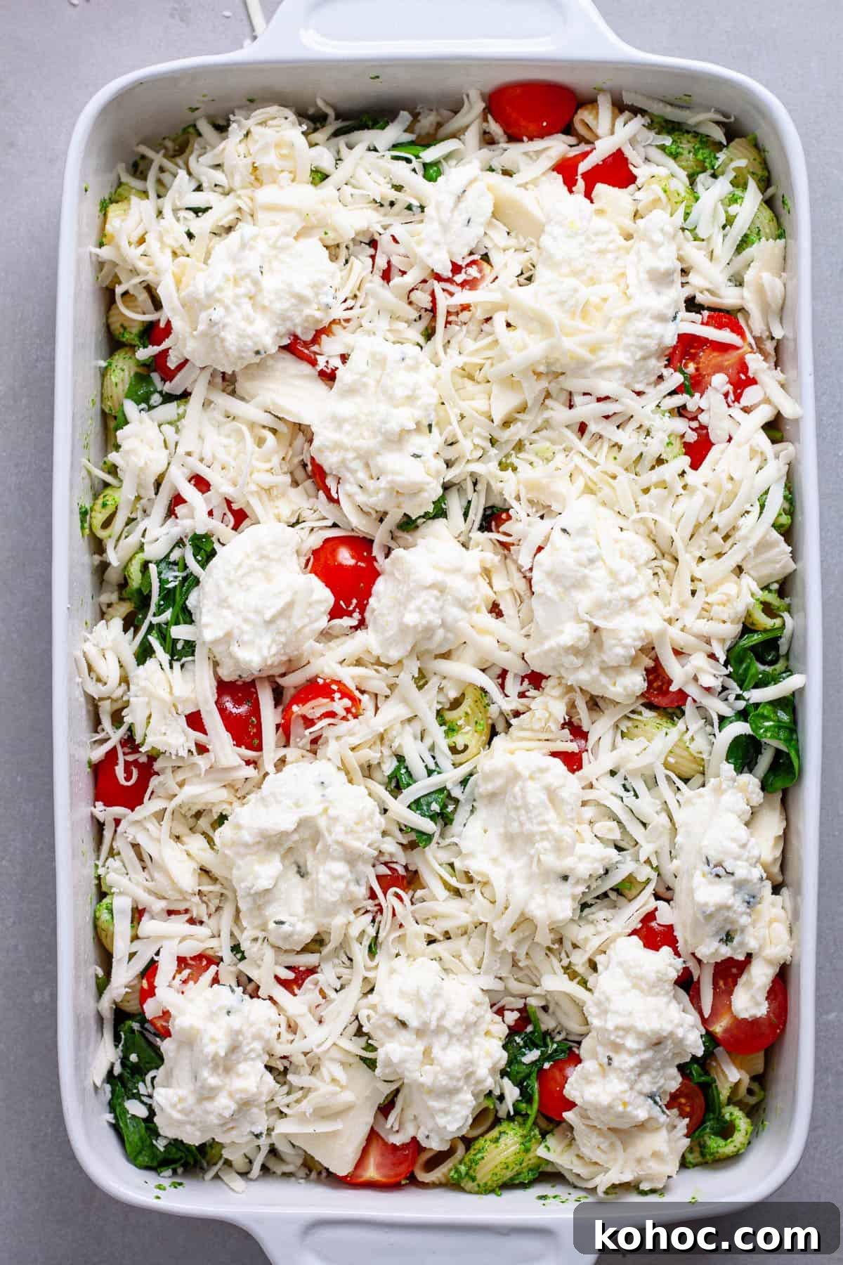 Creamy Baked Ricotta Pesto Pasta with Golden Parmesan Crust 10 A casserole dish of pasta and pesto with ricotta and mozzarella scattered on top, along with tomatoes and spinach.