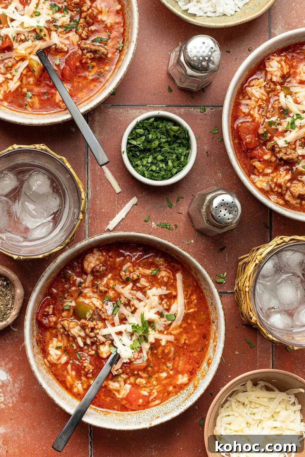 three bowls of stuffed bell pepper soup, small bowl of chopped parsley, glasses of ice water, salt and pepper shakers.
