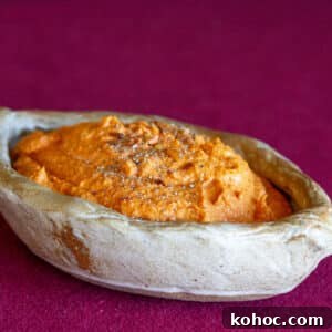 Roasted Red Pepper Hummus Sandwich Recipe for Flavorful Lunch 9 a ceramic dish filled with red pepper hummus on a red background.