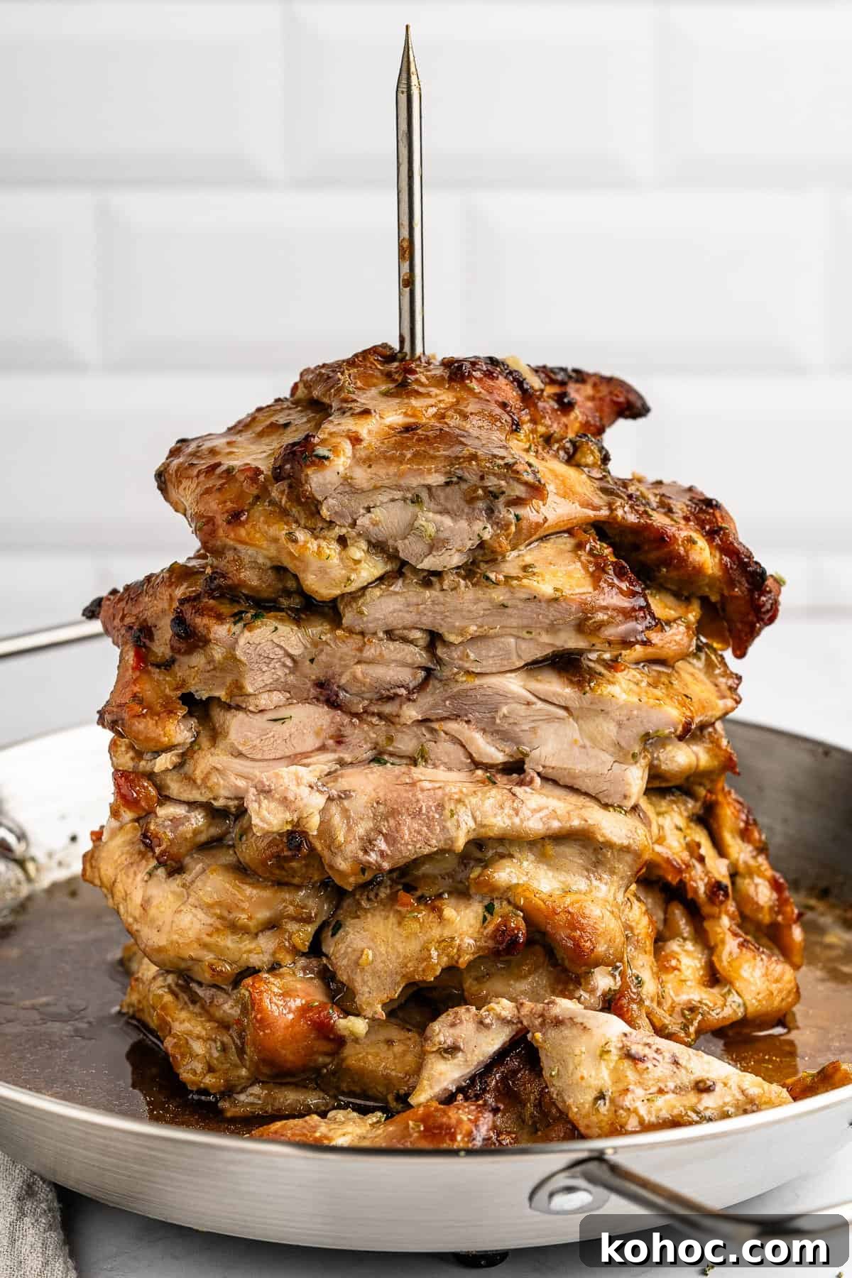 30 High-Protein Dinner Recipes for Muscle & Weight Goals 2 A vertical stack of grilled, seasoned meat slices on a skewer, resembling shawarma or gyro, sits in a metal pan. The high protein gyro is golden brown and juicy, with a crispy outer layer, set against a white tiled background.