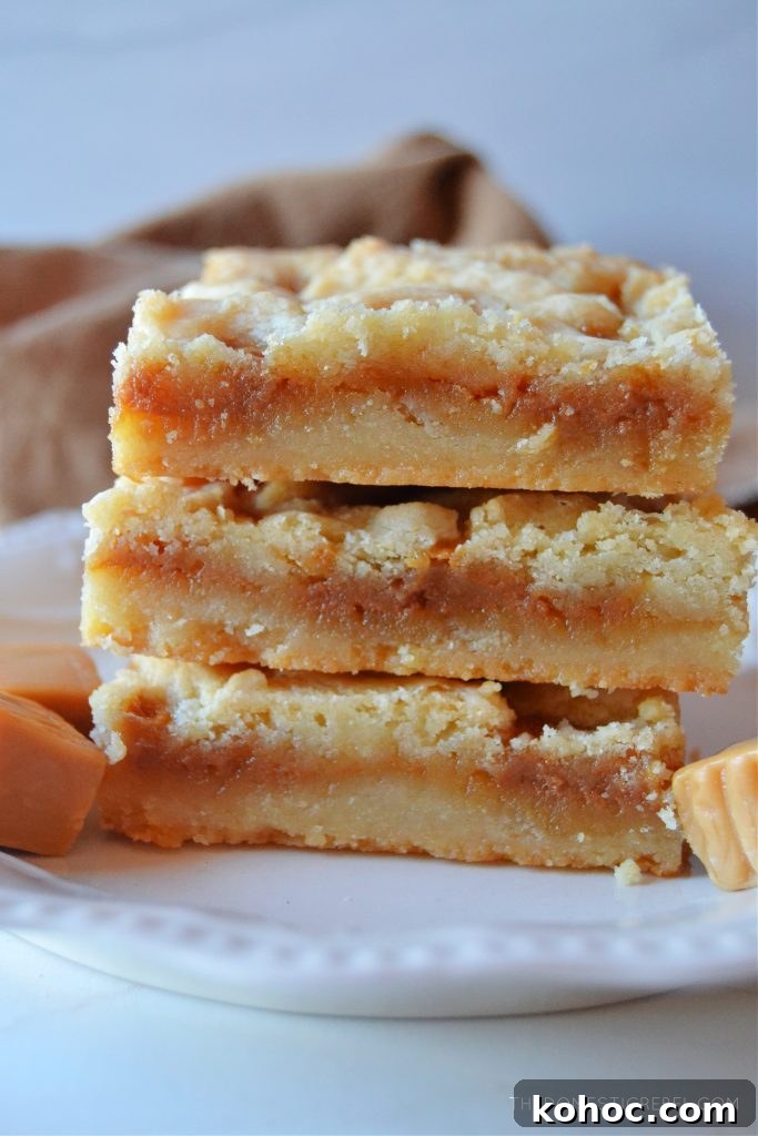 Salted Caramel Butter Bars Recipe with Buttery Shortbread Crust 3 a three-high stack of salted caramel butter bars on a petite white plate next to caramel square candies.
