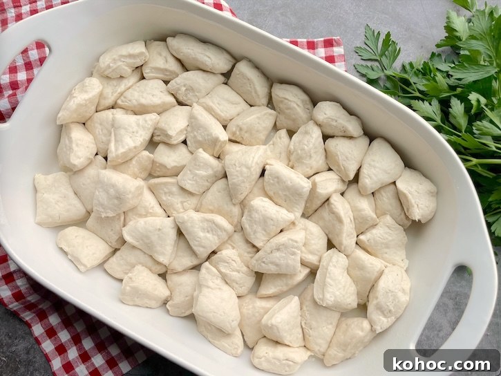 Bubble-Up Biscuit Pizza Casserole Recipe for Family Nights 6 Biscuit dough on the bottom of a 9x13 baking dish ready to be smothered in pizza sauce and shredded mozzarella to make an easy pizza casserole for dinner.