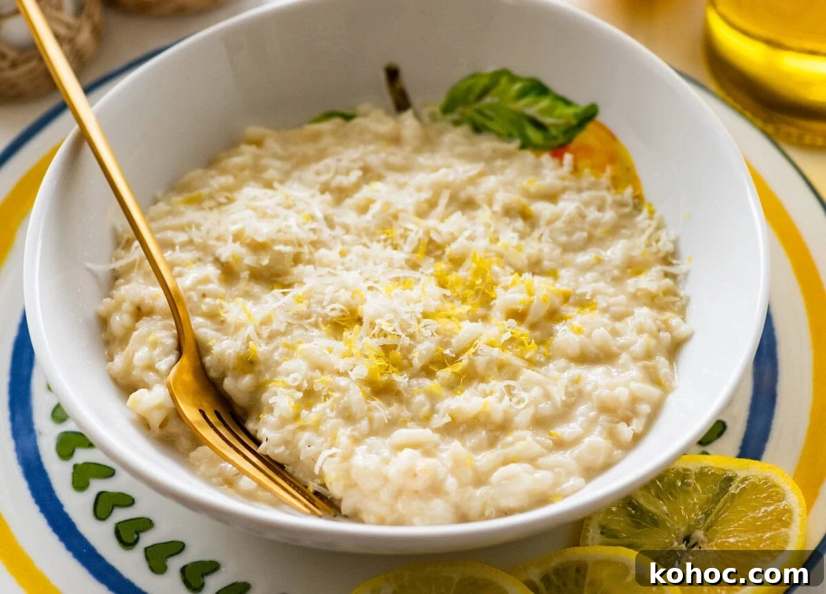 Creamy Lemon Risotto with Parmesan and Fresh Herbs 2 A bowl of lemon risotto with a fork resting in it and lemon slices lined on the edge of the plate.