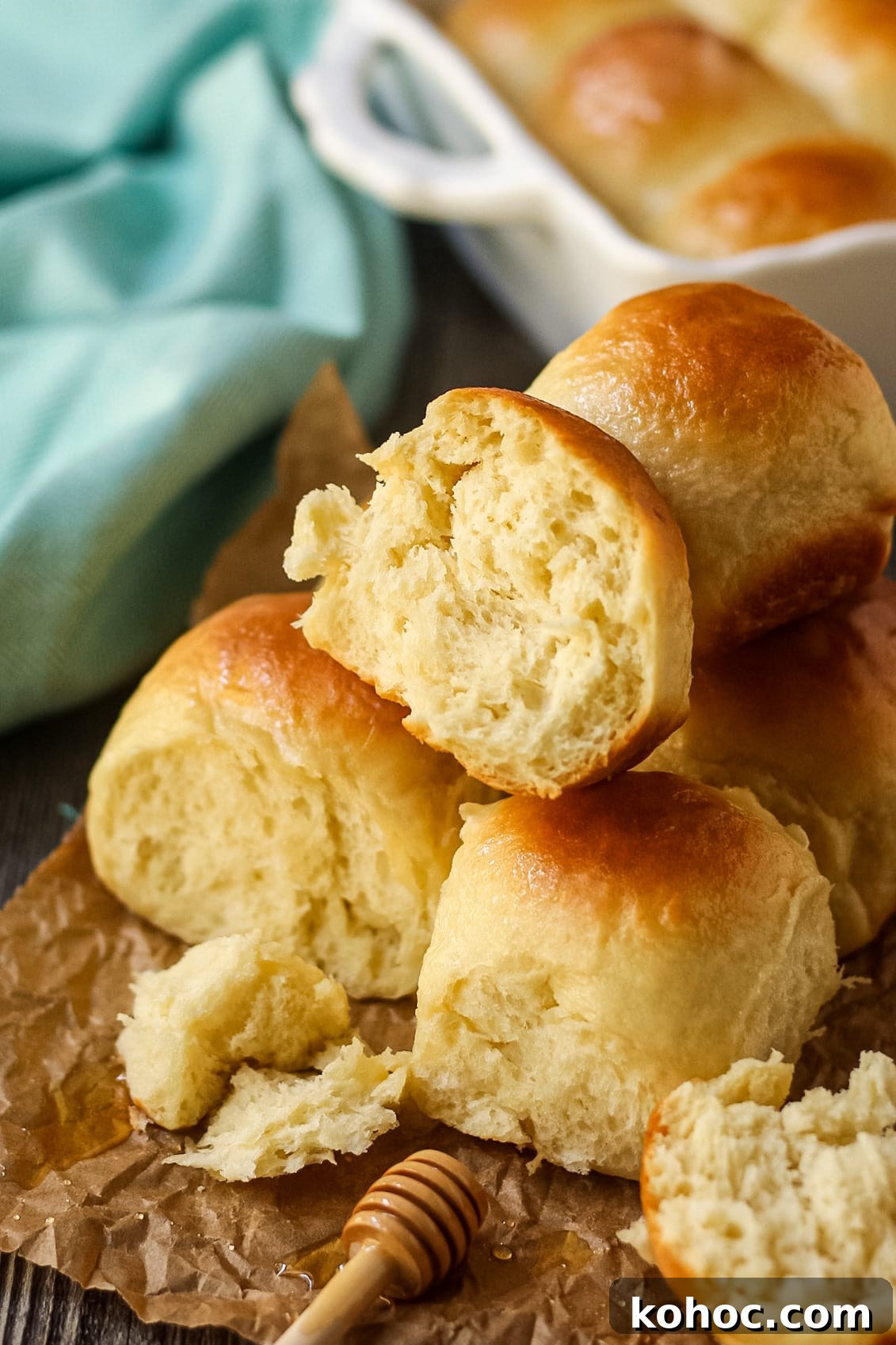 One-Hour Soft and Fluffy Dinner Rolls 2 honey butter dinner rolls on parchment paper. One roll torn open to show texture.