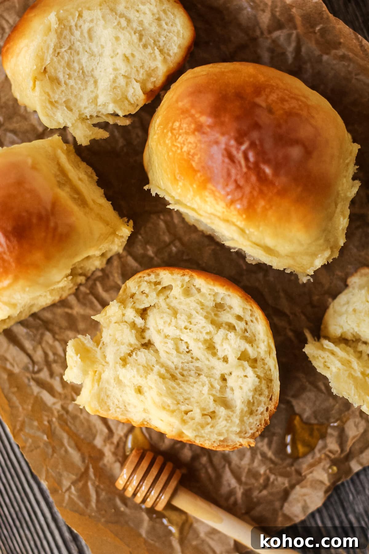 One-Hour Soft and Fluffy Dinner Rolls 4 honey butter dinner rolls on parchment paper. One roll torn open to show texture.