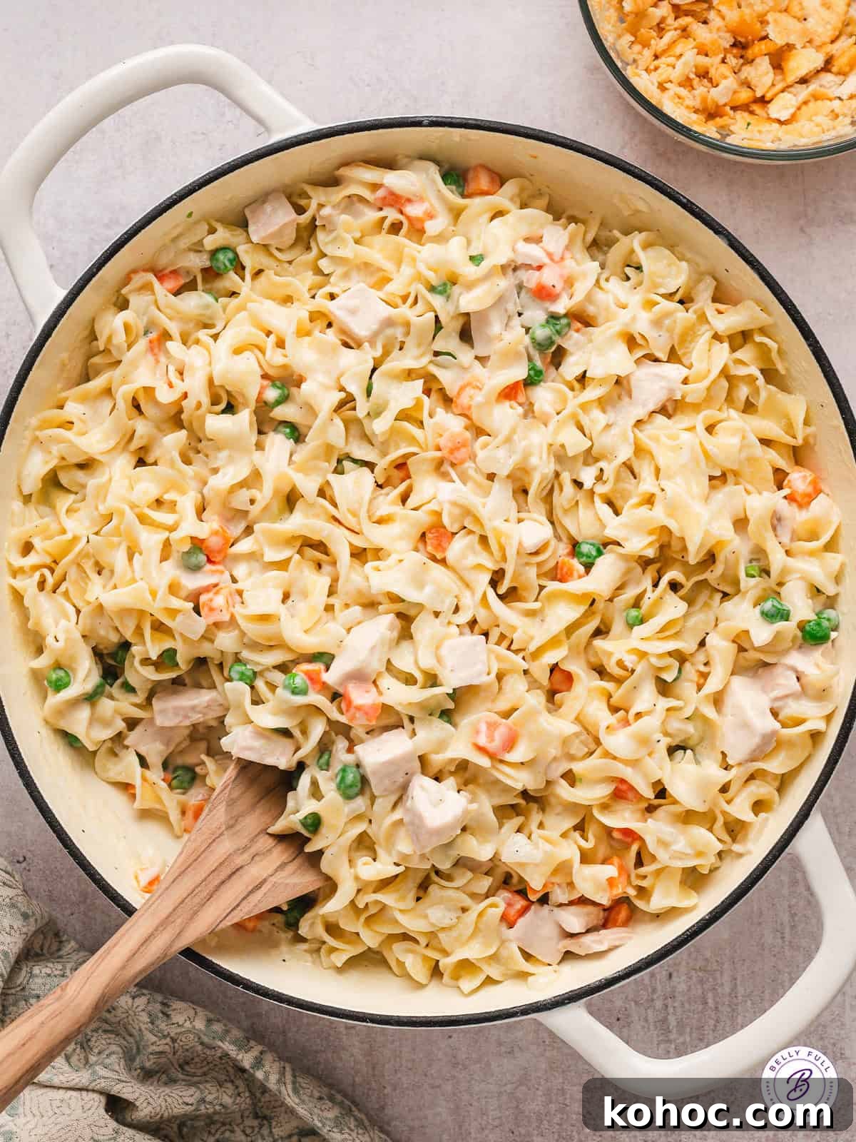 Made with seasoned chicken and egg noodles in a creamy sauce topped with Ritz crackers, Chicken Noodle Casserole is total comfort food. Overhead view of chicken and noodle casserole with a wooden spoon