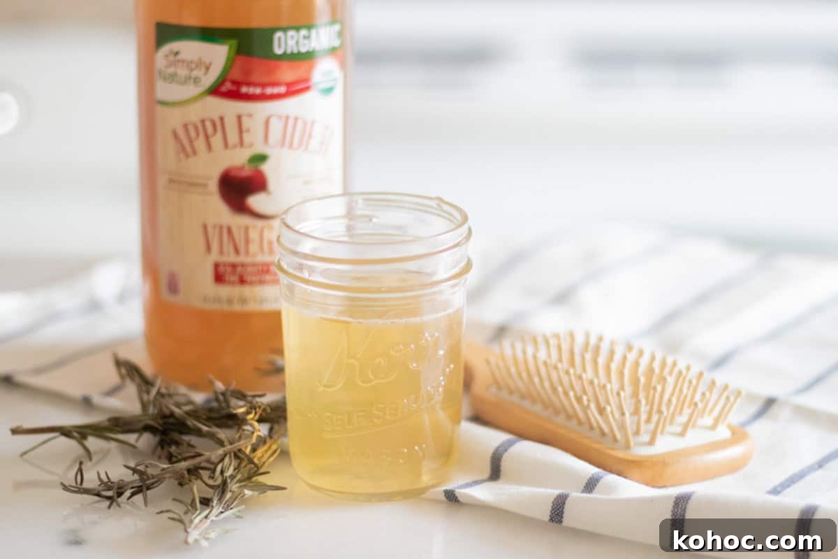 A jar of apple cider vinegar hair rinse with a bottle of apple cider vinegar, a hair brush, and dried rosemary.