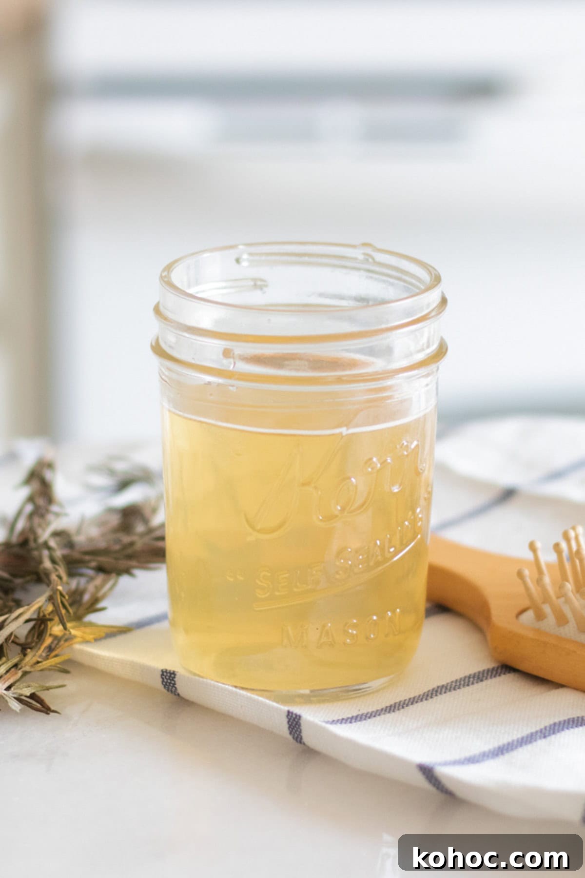 A jar of apple cider vinegar hair rinse on a striped towel with a hair brush.
