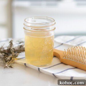 A jar of apple cider vinegar hair rinse with a hair brush and dried herbs.