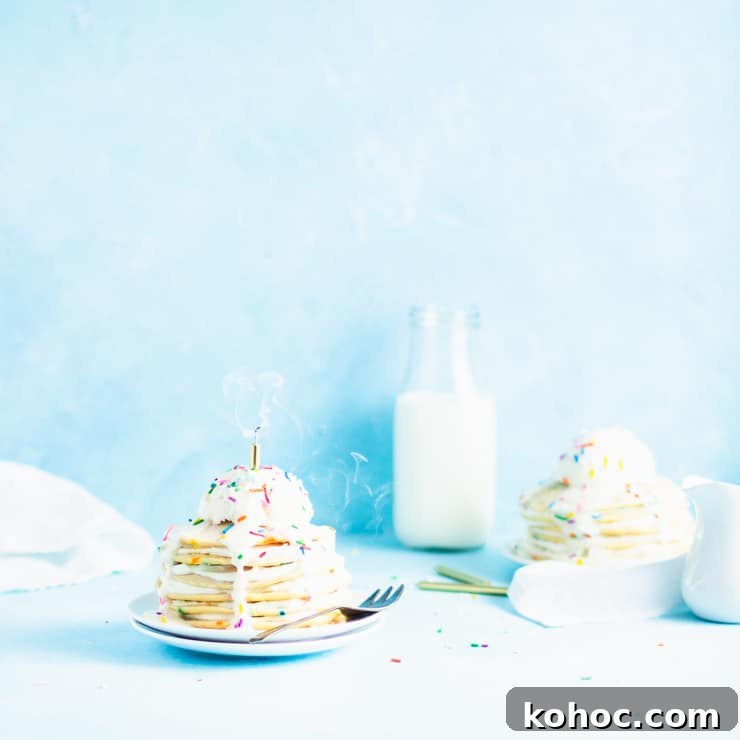stack of pancakes with a freshly blown out candle and swirling smoke with a glass of milk, sprinkles and another stack of pancakes in the background