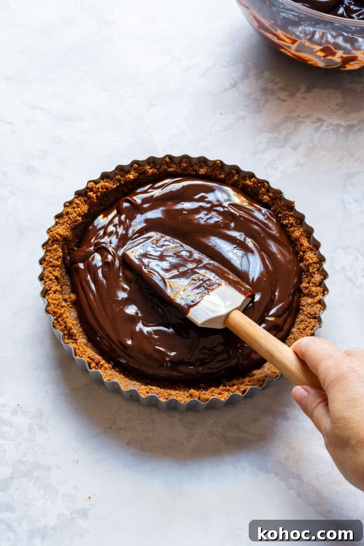 Decadent Chocolate Orange Tart Recipe with Zesty Ganache 8 Spreading dark chocolate ganache into the chilled cookie crust.