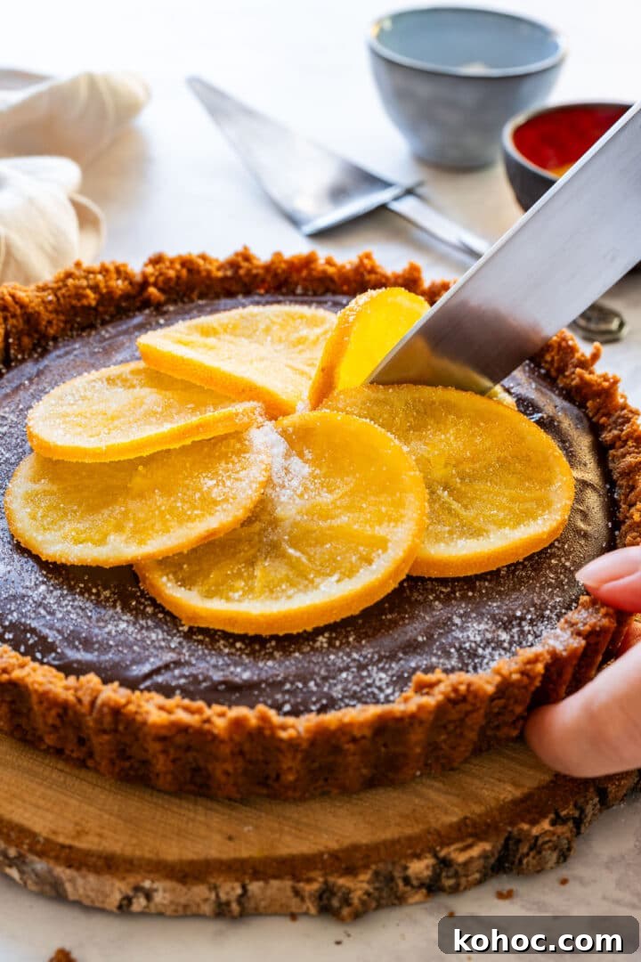 Decadent Chocolate Orange Tart Recipe with Zesty Ganache 10 Slicing the tart topped with candied oranges for serving.