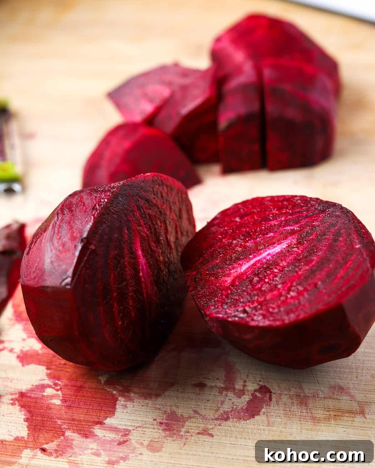 Roasted Beet and Walnut Soup Recipe — Comforting Autumn Starter 3 Photo of a peeled beetroot cut in half with some chopped beetroot in the background, on a wooden chopping board stained with beetroot juices.